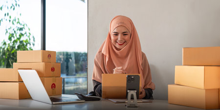 Muslim women selling online at home with box. Selling online with box to accept order from customer. SME business idea. Parcel delivery. muslim woman working smartphone and laptop at homeの写真素材
