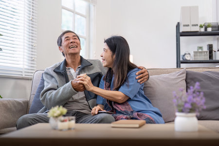Happy mature husband and wife sit rest on comfortable sofa in living room enjoy talking, smiling elderly couple relax on couch at home chat speak laugh on leisure weekendの写真素材