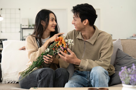 Asian handsome man show the love and give flowers to his girlfriend in living room on valentine day. Lifestyle Conceptの写真素材
