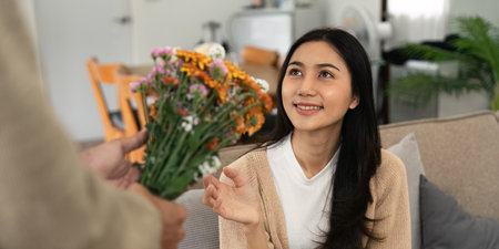 Romantic young asian couple embracing with holding flowers and smiling in living room at home. fall in love. Valentine conceptの写真素材