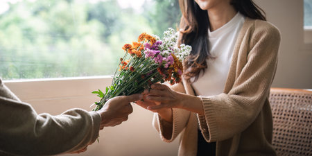 Romantic young asian couple embracing with holding flowers and smiling in living room at home. fall in love. Valentine conceptの写真素材