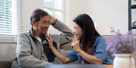 Happy mature husband and wife sit rest on comfortable sofa in living room enjoy talking, smiling elderly couple relax on couch at home chat speak laugh on leisure weekendの写真素材
