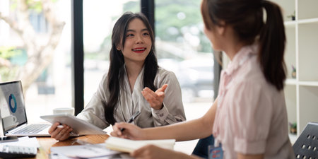 Two Asian businesswoman working with laptop computer and discussing documents and idea at meeting. Teamwork processの写真素材