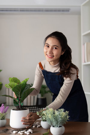 The concept of eco friendly housing, plant care and gardening. Preparing garden. Relax home gardening. Gardener woman asian hand planting flower in pot. Smiling woman takes care of plantの写真素材