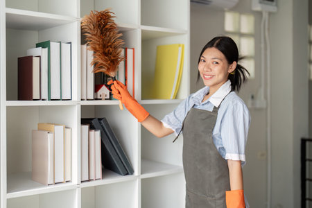 Asian woman clean in office room at office. Housekeeper or maid cleaner feel happy wipe mop and clean your work desk and bookshelf. the office office cleaning staffの写真素材