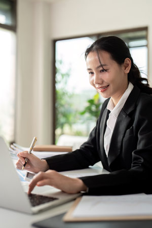 Asian woman accounting sit at their desks and calculate financial graph showing results about their investment, planning successful business growth processの写真素材