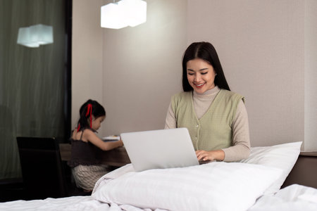 Mom working online at home sharing vacations with little daughter. Funny lifestyle family momentの写真素材