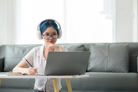 Happy young woman teenage wearing headphones writing note. student online learning class study online video call zoom teacher with laptop and bookの写真素材
