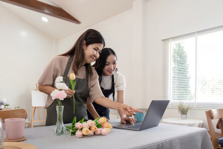 Senior mother and adult daughter happy on the table while arrange flowers in a vase together using laptop computer. lifestyle concept. Happy time togetherの写真素材