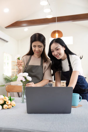 Senior mother and adult daughter happy on the table while arrange flowers in a vase together using laptop computer. lifestyle concept. Happy time togetherの写真素材