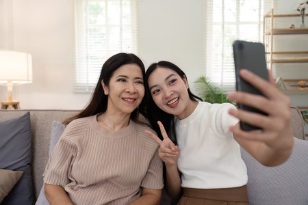 Daughter adult taking selfie using mobile phone with senior mother at homeの写真素材