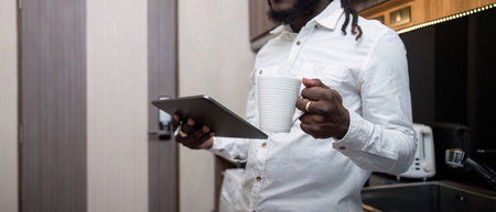 African American man working online on digital tablet and drinking coffee while at kitchen