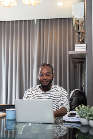 African American man working with laptop computer remote while sitting at glass table in living...