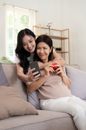 Daughter adult taking selfie using mobile phone with senior mother at homeの写真素材