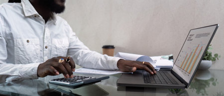 African American man working with laptop computer and using calculator, making financial audit, reviewing bills tax and accounting in living room. Black guy do freelance work at home officeの写真素材