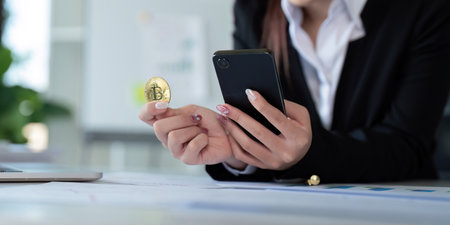 Businesswoman holding a golden bitcoin. using Mobile with graph chart, trading stock market,...