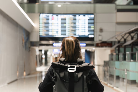 Young woman backpack in international airport terminal looking at the flight schedule information...