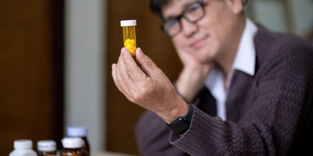 Senior asian man examining prescription medication at homeの写真素材