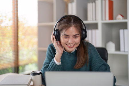 Young woman wearing headphones and smiling while using a laptop in a home office