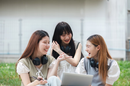 Group of young university students laughing and studying on campus lawn. Friends enjoying outdoor learning and bonding. Concept of education, friendship, and student lifeの写真素材