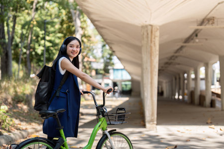 Businesswoman commuting by bicycle with headphones in urban park. Concept of eco friendly transport, active lifestyle, and outdoor fitnessの写真素材