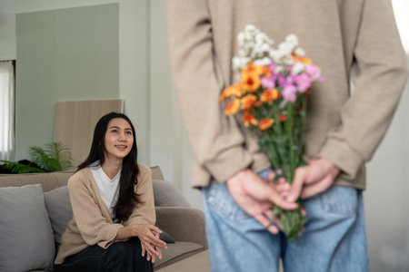Young man surprising woman with flowers at home. Concept of love, affection, and romanceの写真素材