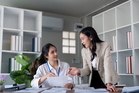 Businesswomen discussing work at office desk. Concept of collaboration, teamwork, and professional discussionの写真素材