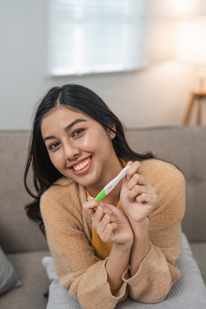 Joyful Woman Holding Positive Pregnancy Test at Home, Celebrating Exciting News with a Bright Smile and Happy Expressionの写真素材