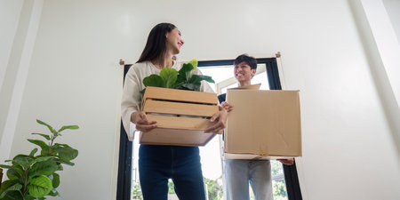 Young Couple Moving into New House Carrying Boxes and Plants, Starting Fresh in Their Modern Home