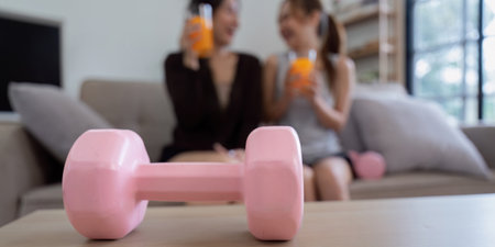 Lesbian Couple Enjoying Healthy Orange Juice Together at Home with Fitness Equipment in the...