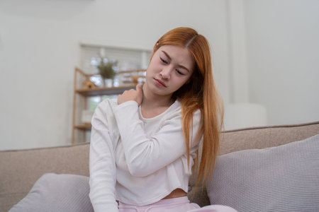 Young Woman Experiencing Neck Pain While Sitting on Couch at Home. Concept of Ache and Pain Flow