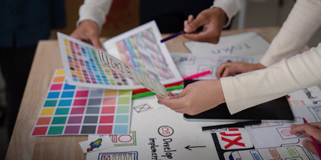 UX Developer and UI Designer Brainstorming Session with Color Palettes and Wireframes on Desk