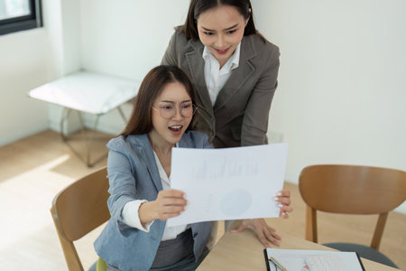 Two Businesswomen Analyzing Financial Report in Modern Office Settingの写真素材