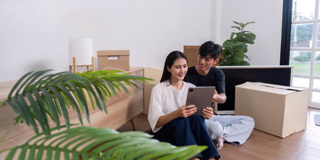 Young Couple Moving into New Home, Unpacking Boxes and Using Tablet to Plan Interior Design in...