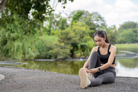 Young Woman Tying Shoelaces in Park Before Exercise, Fitness Enthusiast Preparing for Outdoor...