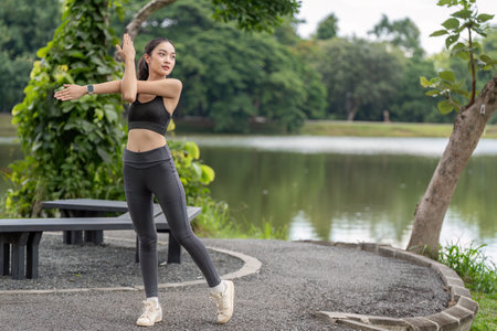 Woman Exercise in Park Wearing Sportswear, Stretching by Lake with Green Trees in Background,...