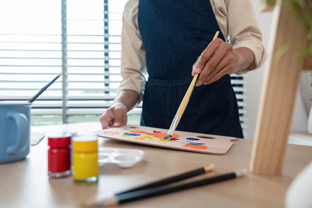 Artist Painting with Brush on Palette in Studio with Art Supplies and Natural Light