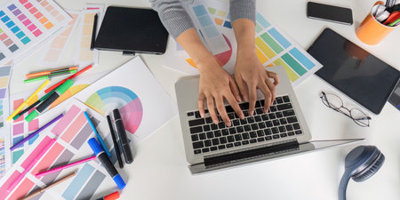 Creative Graphic Designer Working on Laptop with Color Palettes and Design Tools on Desk