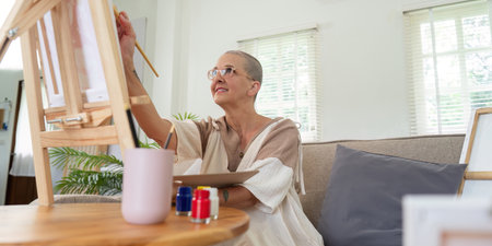 Senior woman painting on easel in cozy home studioの写真素材