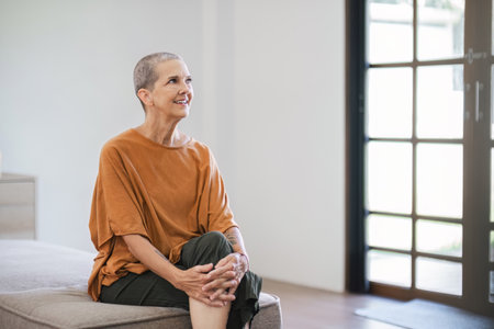 Elderly Woman Sitting on Sofa Smiling in Bright Living Roomの写真素材