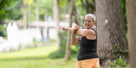 Caucasian senior woman stretching arms in green park before exercise