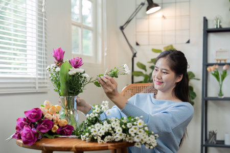 Asian woman creatively arranging flowers in vase at homeの写真素材