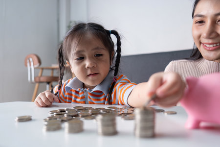 Mother Teaching Daughter Financial Literacy with Coins and Piggy Bankの写真素材