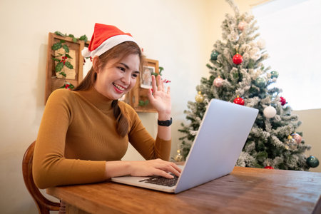 Virtual Holiday Greetings Woman in Santa Hat Waving During Online Callの写真素材