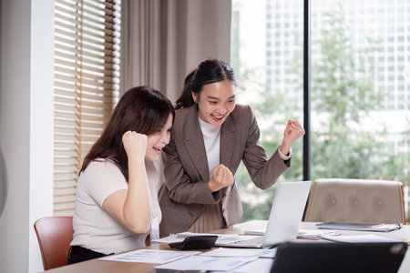 Joyful success for two women in corporate office with laptopの写真素材