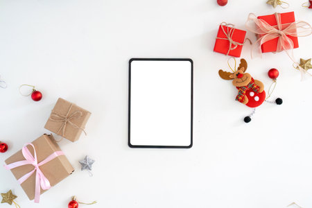 Tablet with Christmas gifts and reindeer ornament on white background.の写真素材
