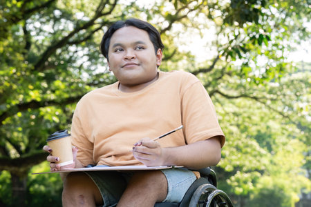 Young Artist in Wheelchair Enjoying Creative Outdoor Session with Coffee in Lush Green Park Settingの写真素材
