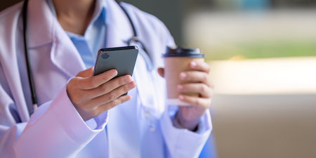 Close up of Asian doctor in lab coat using smartphone and holding coffee