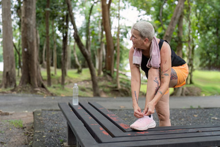 Elderly woman tying her shoelaces on a bench before exercising in a scenic parkの写真素材