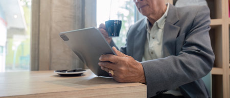 Close-up of senior man sipping coffee while browsing a tablet in a stylish cafeの写真素材